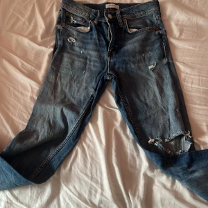 Blå jeans från Zara Woman - Säljer ett par blå jeans från Zara Woman Premium Denim Collection. De har en cool distressed look med flera slitningar och är i en klassisk blå färg. Perfekta för en avslappnad och trendig stil! Dom är straight lågmidjade på mig