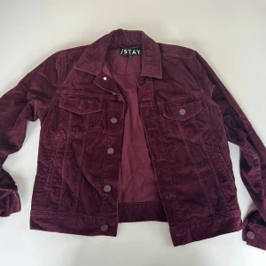 Vinröd manchesterjacka från Stay - Säljer en snygg vinröd manchesterjacka från Stay. Jackan har en klassisk design med knappar framtill och två bröstfickor. Perfekt för höst och vår!