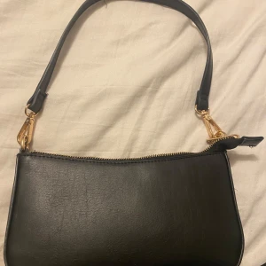 Svart väska - Svart väska med guld dragkedja  One size Välanvänd  Har ingen aning vart jag köpte den, men tror det är new yorker Utsidan är 100% polyuretan  Insidan är 100% polyester  