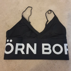 Svart sporttopp från Björn Borg - Säljer en snygg svart sporttopp från Björn Borg. Den har smala axelband och ett brett resårband med Björn Borg-loggan i vitt. Perfekt för träning eller en avslappnad dag. Ny! storlek s.