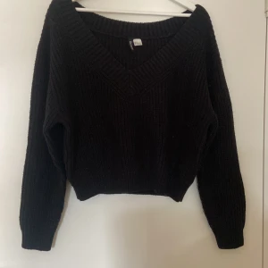 Svart stickad tröja från H&M Divided - Säljer en svart stickad tröja från H&M Divided. Den har en djup v-ringning och långa ärmar, perfekt för höst och vinter. Tröjan är i storlek M och har en mysig, ribbad textur. Perfekt för att hålla sig varm och stilren under kyliga dagar!