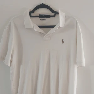 Vit pikétröja från Ralph Lauren - Säljer en klassisk vit pikétröja från Ralph Lauren i storlek L. Tröjan är gjord av mjuk Pima-bomull och har den ikoniska broderade loggan på bröstet. Perfekt för en stilren och avslappnad look!