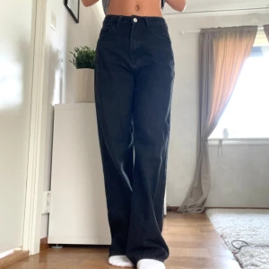 Svarta vida byxor - Säljer ett par svarta byxor med hög midja och en vid passform. De är perfekta för en avslappnad men stilren look. Byxorna har knappar och dragkedja framtill.
