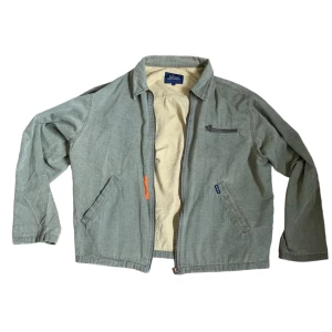 Grön jacka från Peak Performance - Säljer en grön jacka från Peak Performance i storlek L. Jackan har en dragkedja framtill och flera praktiska fickor, inklusive en bröstficka med dragkedja. Den är perfekt för vår och höst med sin stilrena design och bekväma passform.