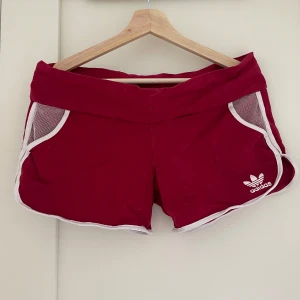 Röda shorts från Adidas - Snygga röda shorts från Adidas. De har en vit kant och meshdetaljer på sidorna.  Adidas-loggan syns både fram och bak. 