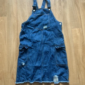 Jeansklänning från Name It - Cool jeansklänning från Name It i storlek 158. Har slitna detaljer och justerbara axelband. Perfekt till hösten! Den har även fickor och en rå kant nertill. Inga synliga defekter! 💙