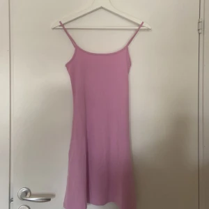 Ljusrosa klänning från H&M Divided - Säljer en superfin ljusrosa klänning från H&M Divided. Den är ärmlös med smala axelband och har en enkel, stilren design. Perfekt för sommardagar eller som en söt vardagsklänning. Materialet känns mjukt och bekvämt mot huden. Passar perfekt för en avslappnad look!