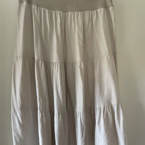 Beige långkjol med volanger - Säljer en superfin beige långkjol med volanger. Kjolen har en mjuk och bekväm passform, perfekt för både vardag och fest. Den är i ett lätt och luftigt material som gör den idealisk för vår och sommar. Passar perfekt med en enkel topp eller blus!