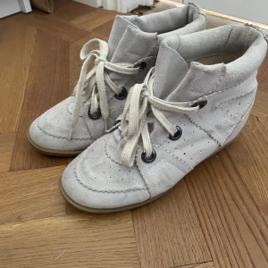 Vita sneakers från Isabel Marant - Säljer ett par snygga vita sneakers från Isabel Marant. De har en cool design med snörning och perforerade detaljer. Skorna är i mocka och har en bekväm passform. Perfekta för både vardag och fest! köpt begagnad utan äktighetsbevis och har därmed inga. tror även att det är en gammal modell på de med tanke på färgen. super coola fortfarande!