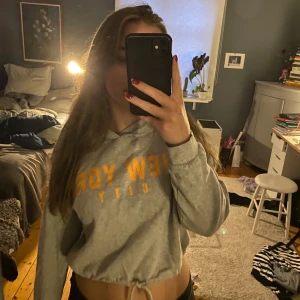 Grå hoodie från H&M med New York City-tryck - Säljer en supermysig grå hoodie från H&M med oranget tryck på framsidan, man kan dra åt den där nere för att justera passformen också🫶🏻🫶🏻