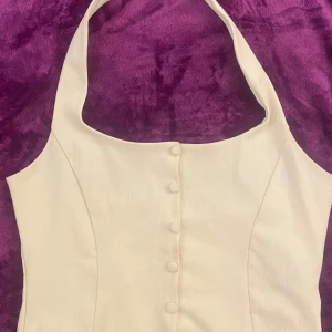 Vit klänning från Gina Tricot - Snygg vit top  från Gina Tricot med knappar framtill och halterneck-design. Perfekt för sommarens alla tillfällen. Klänningen har en stilren och elegant look.