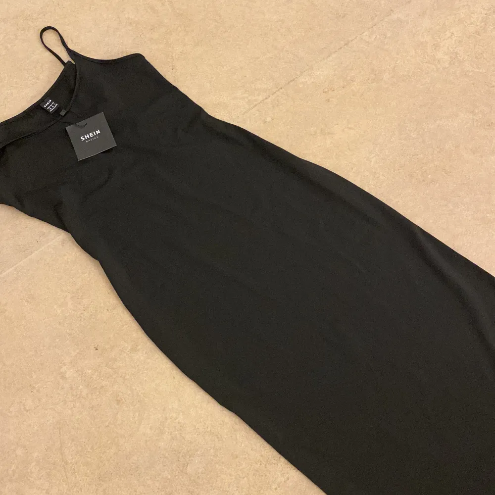 Elegant svart långklänning från Shein med smala axelband. Perfekt för en stilren look. Klänningen har en figurnära passform som framhäver silhuetten.. Mekot.