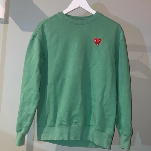 Grön sweatshirt med broderat hjärta - Säljer en grön sweatshirt från H&Mmed ett broderat rött hjärta på bröstet. Tröjan har långa ärmar och en avslappnad passform. Perfekt för en casual look. Tröjan är Xs men passar mer S
