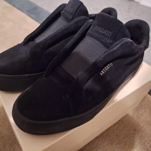 Svarta sneakers från Axel Arigato 360 laceless 39 - Jag säljer ett par Axel arigato i en jätte bra skick I storlek 39 men den är stor I storleken så den kan passa 40 och kanske 41. Nytt pris ligger på 2550 men är  slutsålda typ överallt. Det är  Snygga svarta sneakers från Axel Arigato i mocka. De har en stilren design med diskret logga på sidan och elastiska band över foten för en bekväm passform. Perfekta för en minimalistisk look. 
