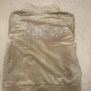 Beige velourjacka från Juicy Couture - Säljer en beige velourjacka från Juicy Couture med glittrande Juicy-logga på ryggen. Jackan har dragkedja framtill och två fickor med dragkedjor. Perfekt för en avslappnad och stilren look.