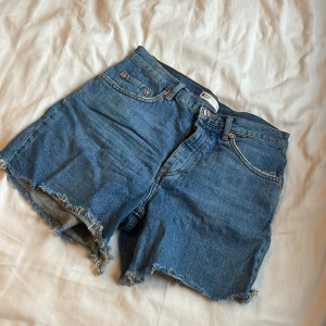 Blå jeansshorts med fransar - Säljer ett par coola blå jeansshorts med fransiga kanter. Perfekta för sommardagar och festivaler. De har en klassisk femficksdesign och knappgylf. Använd en gång 