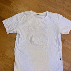 Kenzo Paris T-shirt - Snygg vit t-shirt från Kenzo med ett coolt tigertryck i mitten. Perfekt för en avslappnad stil med en touch av lyx. T-shirten har en normal passform och korta ärmar.