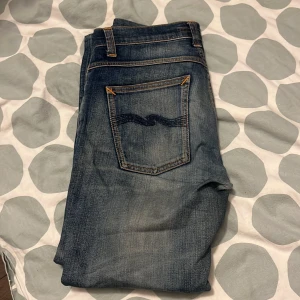 Blå jeans från Nudie Jeans - Säljer ett par snygga blå jeans från Nudie Jeans. De har en klassisk femficksdesign och en normal passform. Jeansen har en lätt tvättad look med subtila slitningar för en cool stil. Perfekta för en avslappnad vardagslook.