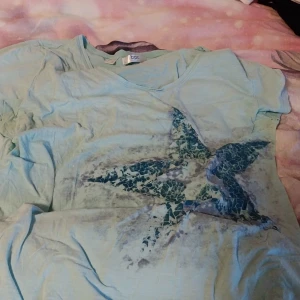 Ljusblå t-shirt med stjärnmönster - Säljer en ljusblå t-shirt från GAP med ett coolt stjärnmönster i mosaikstil på framsidan. T-shirten har en v-ringad hals och korta ärmar. Perfekt för en avslappnad stil!