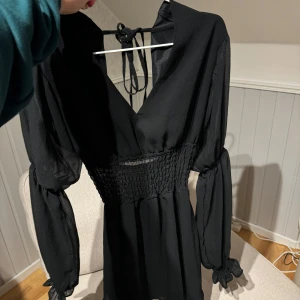 Svart klänning med knytband - Svart klänning med v-ringning och öppen i ryggen. Från NAKD, använd 1-2 gånger och är i nyskick. 