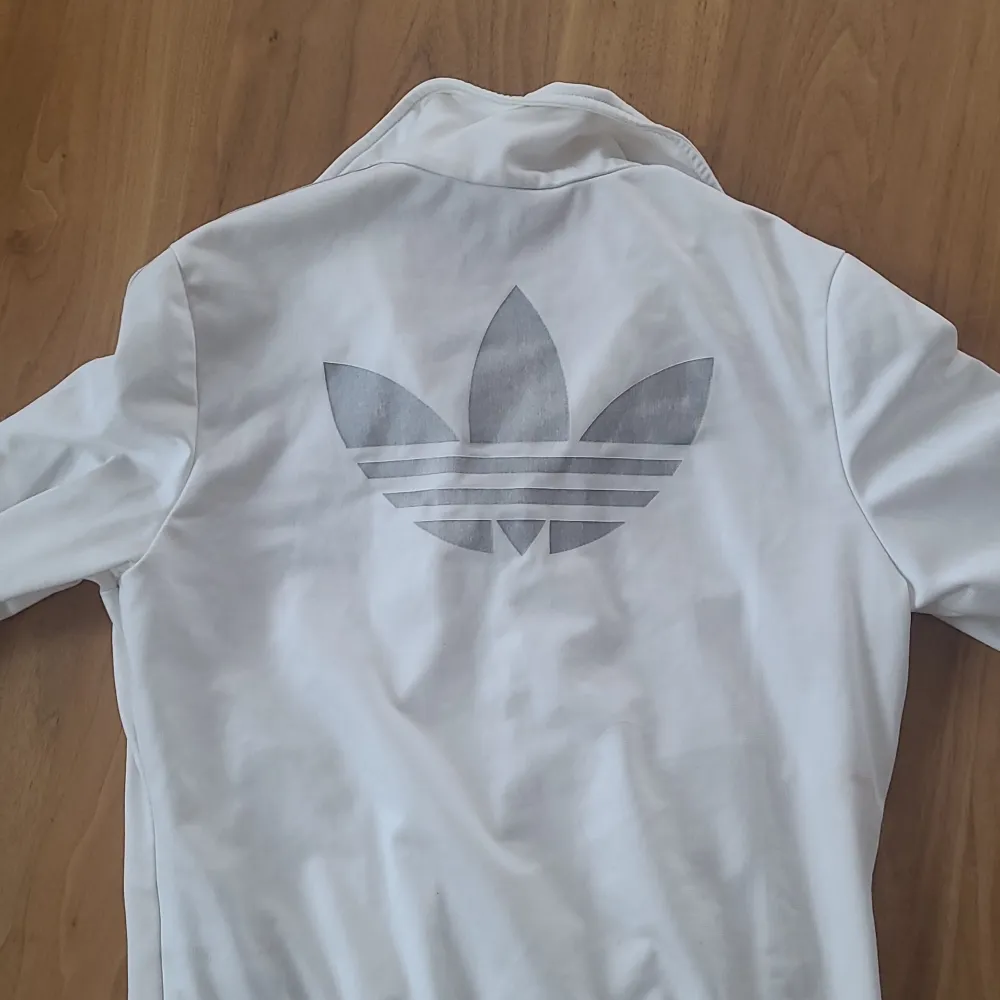 Säljer en stilig vit jacka från Adidas med dragkedja och ribbade muddar. Jackan har långa ärmar och ett stort Adidas-logotyp på ryggen. Har inga tydliga tecken på slitage men finns 2 fläckar av något blått(se sista 2 bilderna) som inte syns när man har på sig koftan. . Neuletakit & Villapaidat.