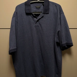Mörkblå pikétröja från George - Snygg mörkblå pikétröja från George med klassisk krage och korta ärmar. Perfekt för en avslappnad stil. Tröjan har ett diskret rutmönster som ger en stilren look.