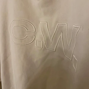 Beige sweatshirt från C.W. - Säljer en stilren beige sweatshirt från C.W. med broderad logga på framsidan. Tröjan har långa ärmar och en rund halsringning med ribbade muddar.