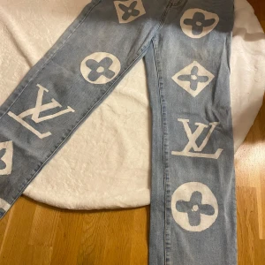Ljusa jeans med tryck från Seventh Heaven - Unika ljusblå jeans med stort vitt tryck av olika symboler. De har en klassisk femficksdesign och knappgylf. Perfekta för dig som vill sticka ut med en cool och trendig stil. 