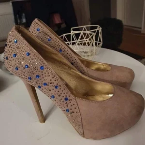 Beige pumps med blå och guld detaljer - Eleganta beige pumps med hög klack och dekorativa blå och guld pärlor. Perfekta för att ge en glamorös touch till din outfit.