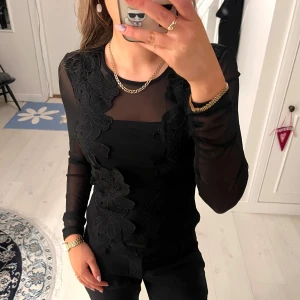 Svart mesh topp - Svart långärmad topp från Vila med mesh ärmar och blommiga spetsdetaljer framtill. Toppen är aldrig använd och lappen sitter kvar. Pris kan alltid diskuteras❤️