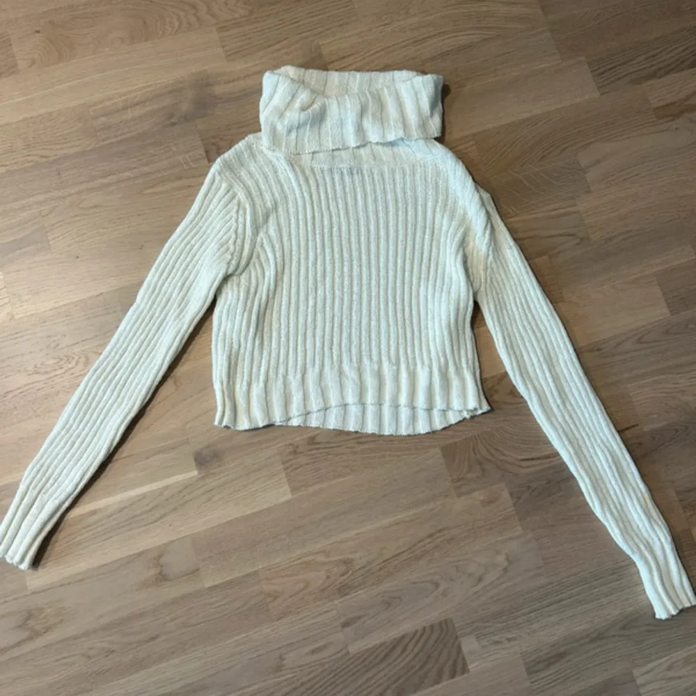 Säljer en stilren vit ribbad polotröja med långa ärmar. Perfekt för kyligare dagar med sin mysiga polokrage. Tröjan har en klassisk design som passar till många olika outfits.. Neuletakit & Villapaidat.