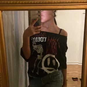 Svart offshoulder t-shirt med tryck - 💕Cool svart t-shirt med offshoulder-design och tryck av skelett, text och flammor. Perfekt för en edgy look med unika detaljer som ger en rockig känsla. Klippte bort ”kragen” så att tröjan blev en off the shoulder💕