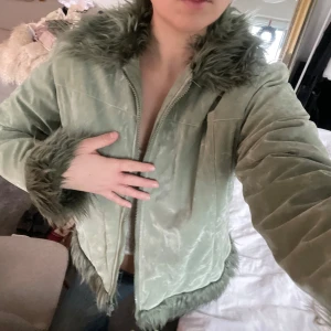 Grön jacka med fuskpälsdetaljer - Snygg grön jacka med dragkedja och fuskpälsdetaljer vid krage, ärmslut och nederkant. Perfekt för att hålla sig varm och stilren under kyligare dagar.