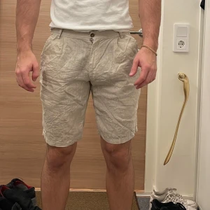 Beige linne shorts - Säljer ett par bekväma beige shorts i linne. De har en normal passform med knappar och dragkedja framtill. Perfekta för varma sommardagar!