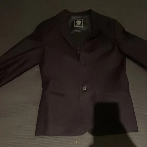 Svart kavaj från Dal Lago - Elegant svart kavaj från Dal Lago i 100% ull. Perfekt för formella tillfällen med en klassisk design och knappar framtill. Kavajen har en stilren look och är tillverkad med högkvalitativt material för en bekväm passform. Storlek 12 år/152. Nypris 4500