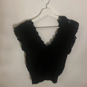 Svart spetsblus - Snygg svart blus med spetsdetaljer och v-ringning. Perfekt för en elegant look. Blusen har korta ärmar och en feminin design.