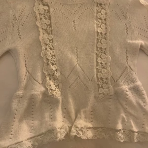 Vit stickad tröja från Zara - Säljer en söt vit stickad tröja från Zara med vackra spetsdetaljer framtill och vid fållen. Tröjan har ett fint mönster, perfekt för en romantisk look. Passar bra till både jeans och kjol!