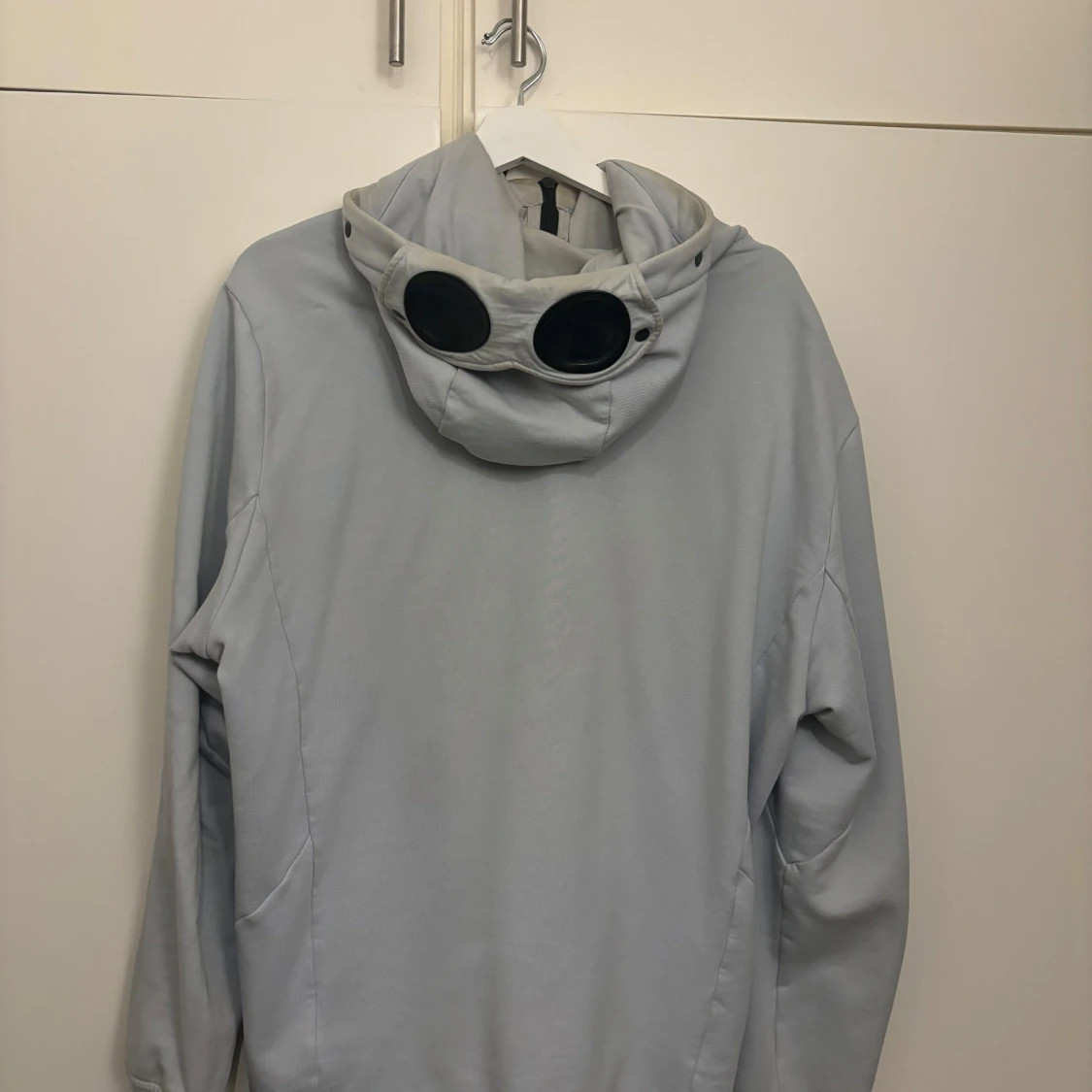 Ljusgrå jacka med huva och glasögondetalj