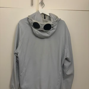 Ljusgrå jacka med huva och glasögondetalj - Snygg ljusgrå jacka med unik glasögondetalj på huvan. Perfekt för en stilren look. Jackan har långa ärmar och dragkedja framtill.