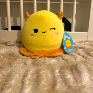 Gul Alien Squishmallow Bijan - Säljer en supermjuk och gosig gul Squishmallow vid namn Bijan. Den har ett sött ansikte med ett blinkande öga och små horn. Perfekt för samlare eller som en mysig kudde. Kommer med originaletikett. Köpt för inte alls länge sen inga defekter va ja sätt❤️
