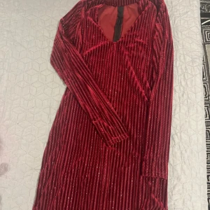Röd glittrig klänning - Snygg röd klänning med glittriga detaljer och långa ärmar. Klänningen har en v-ringad design och en dragkedja i ryggen. Perfekt för en festlig kväll!