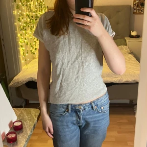 Grå t-shirt med öppen rygg från Zara - Snygg grå t-shirt från Zara med en unik öppen ryggdetalj som knyts. Perfekt för en avslappnad stil med en twist. Kortärmad och tillverkad i mjukt material för extra komfort.