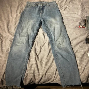 Blå jeans från Tiger of Sweden - Säljer ett par klassiska blå jeans från Tiger of Sweden. De har en straight passform och är tillverkade i slitstarkt denim. Perfekta för en avslappnad stil. Jeansens läderpatch med logotypen ger en snygg detalj. Osäker på storlek, men skulle tippa på 34/36