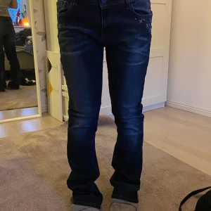 Mörkblå jeans från Blue Fire Co - Snygga mörkblå jeans från Blue Fire Co med dekorativa detaljer vid fickorna. Jeansen har en klassisk femficksdesign och en bekväm passform. Perfekta för en stilren look. Ganska långa i modellen