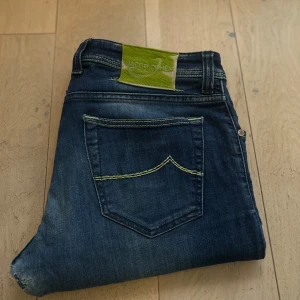 Jacob Cohen - Snygga blå jeans från Jacob Cohen med en cool tvätt och kontrastsömmar i grön färg. De har en klassisk femficksdesign och en grön etikett bak med Jacob cohen loggan. Otroligt sköna att använda och är väldigt snygga. Nypris på dessa ligger runt 5-6 tusen kronor. Negativt är att de finns lagning i skrevet ( syns inte vid användning ) och sedan att det har skavts bort lite på etiketten där bak. Vid frågor eller funderingar är det bara att skriva // mvh Elias 