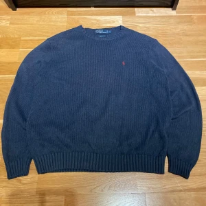 Blå stickad tröja från Polo Ralph Lauren - Säljer en snygg blå stickad tröja från Polo Ralph Lauren i storlek L. Tröjan är tillverkad i 100% bomull och har en röd broderad logotyp på bröstet. Perfekt för kyligare dagar med sin ribbade design vid ärmslut och nederkant.
