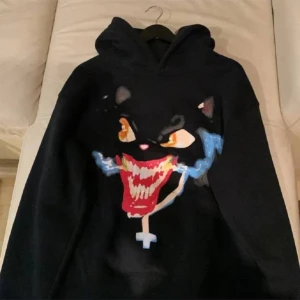 Svart hoodie med kattmotiv - Cool svart hoodie med ett stort kattmotiv i färgglada nyanser på framsidan. Baksidan har en tryckt lista med olika städer och datum. Perfekt för en avslappnad stil.