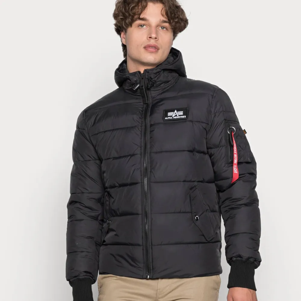 Snygg svart pufferjacka från Alpha Industries med huva och dragkedja. Jackan har en broderad logga på bröstet och en röd detalj på ärmen. Perfekt för kyliga dagar. Skriv för mer bilder, och skick osv 😁. Takit.