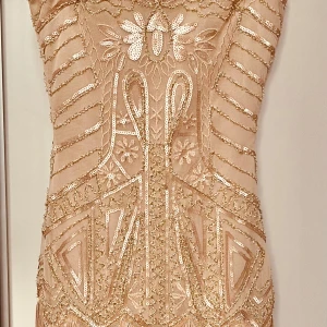 Champagnefärgad klänning från Babeyond - Säljer en elegant champagnefärgad klänning från Babeyond. Klänningen är dekorerad med glittriga paljetter och har ett intrikat mönster. Perfekt för en glamorös kväll.