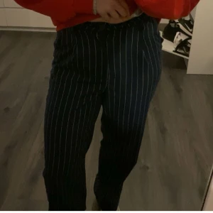 Randiga kostymbyxor - Snygga kostymbyxor med vita ränder på en mörkblå bas. Byxorna har en klassisk passform och är perfekta för en stilren look. De är högmidjade och ger en elegant siluett.